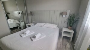 Ein Hotelzimmer mit einem großen Bett, zwei Nachttischen, einem Spiegel, einer Lampe und einer Zimmerpflanze.