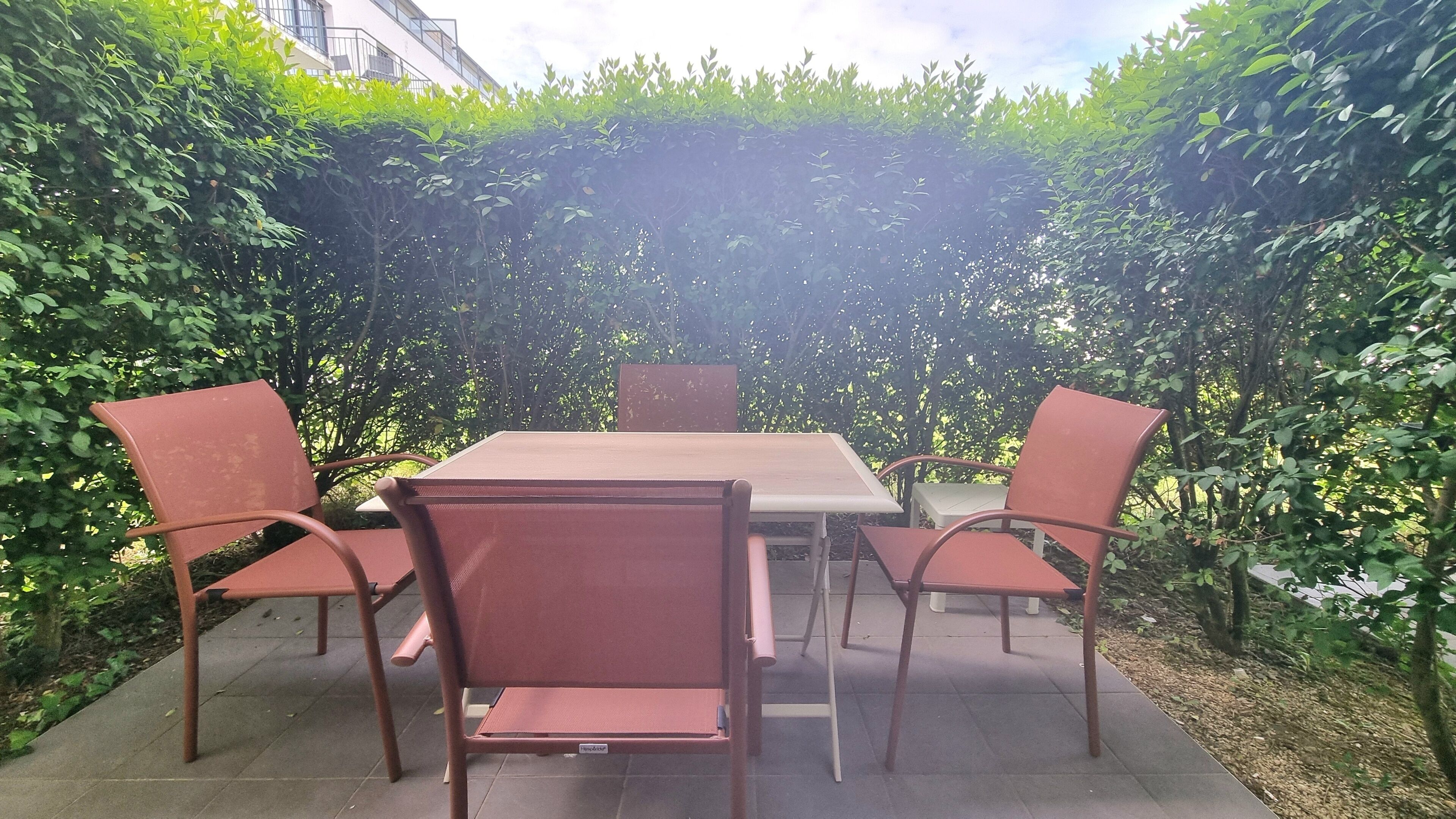 Une terrasse extérieure avec une table et quatre chaises, entourée d’une végétation luxuriante.