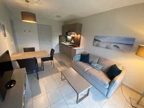 A compact living space with a dining area, kitchenette, and a sofa with cushions.