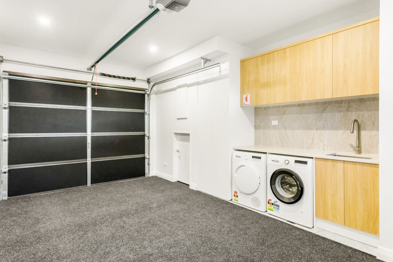 A compact laundry room with a washing machine and dryer, a small sink, and a garage door.