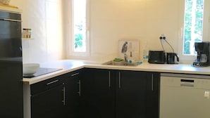 A modern kitchen with dark cabinets, a dishwasher, a sink, and a window providing natural light. - Gite 4 Personnes Terrasse Jardin Piscine (aspiran)
