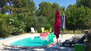 A swimming pool with inflatable toys, lounge chairs, and umbrellas. - Gite 4 Personnes Terrasse Jardin Piscine (aspiran)