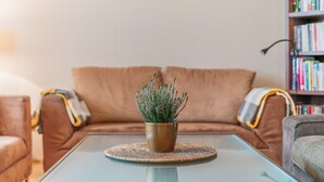 Un salón con un sofá marrón, una mesa de centro de vidrio con un posavasos tejido, y una pequeña planta en maceta.