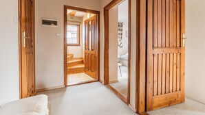 Un pasillo con puertas de madera, suelo alfombrado y vistas a un dormitorio con cama y ventana.