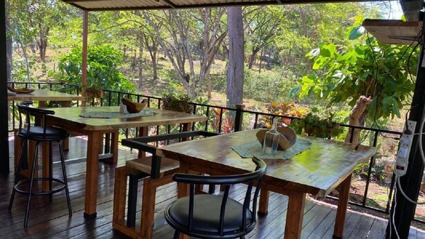 An outdoor wooden deck with tables and chairs, surrounded by lush greenery. - Nueva Villa Paraiso (Lagunillas)