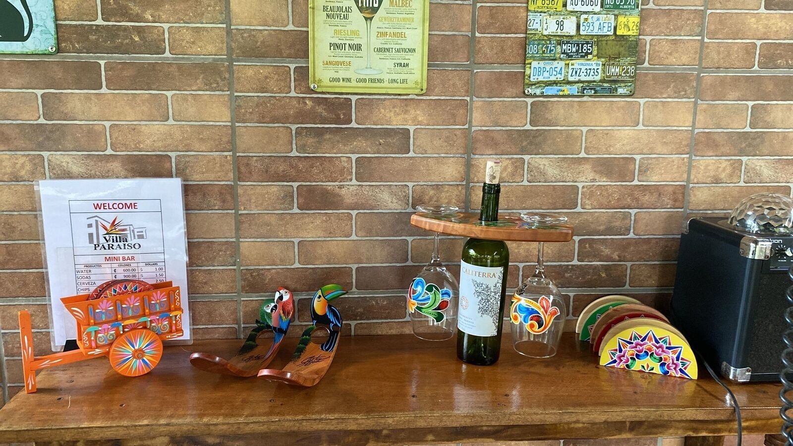 A bar area with a wooden counter, a mini bar menu, colorful bird-shaped glasses, a bottle of wine, and a vintage jukebox.