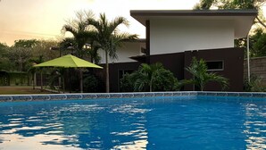 A swimming pool with a tiled edge, surrounded by palm trees and a modern building with a flat roof. - Nueva Villa Paraiso (Lagunillas)