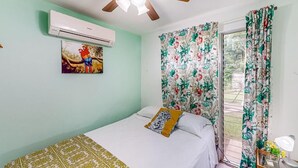 A bedroom with a bed, a ceiling fan, an air conditioner, a window with floral curtains, and a wall-mounted air conditioner. - Nueva Villa Paraiso (Lagunillas)