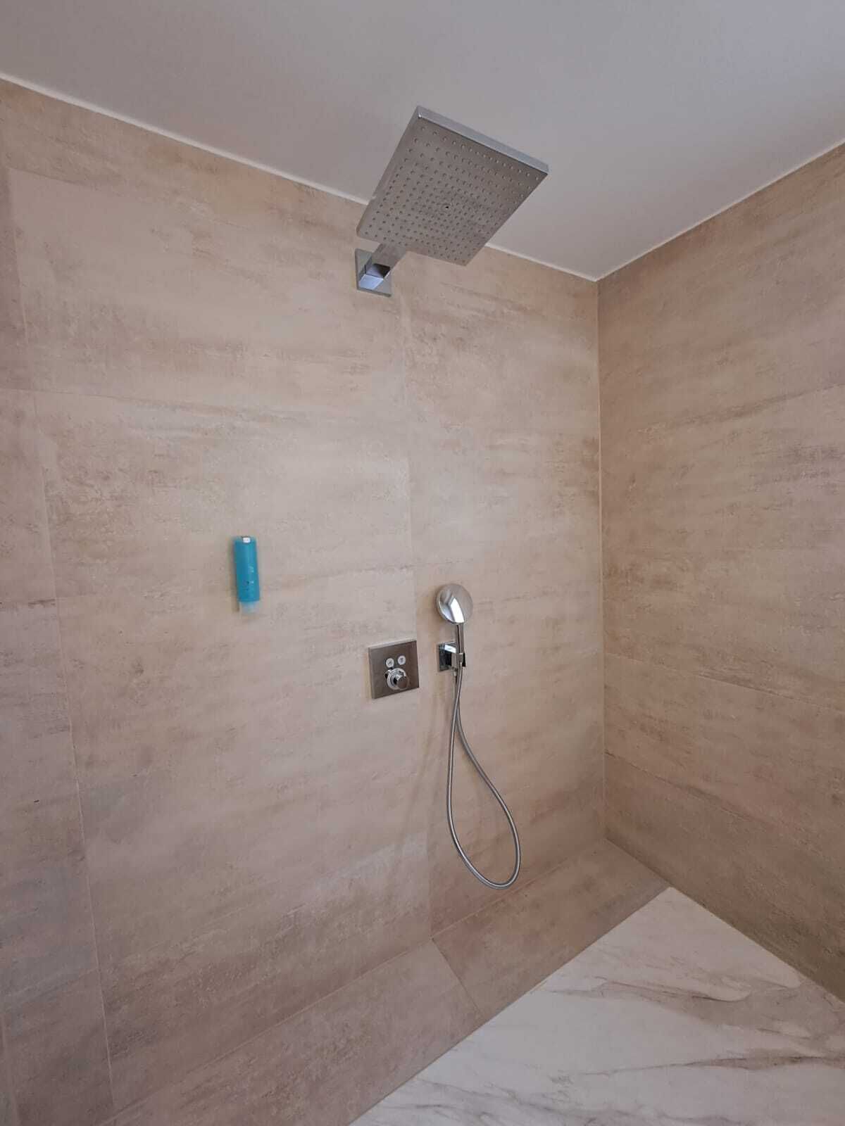 A shower with a handheld showerhead and a wall-mounted control panel.