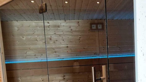 Un baño moderno con paneles de madera, cabina de ducha de vidrio y un reloj visible en la pared.