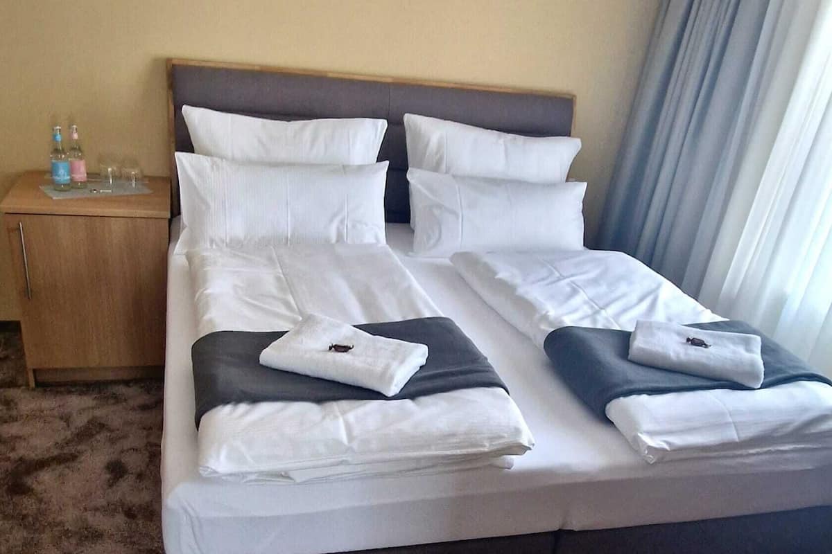 Un lit bien fait, avec une literie blanche et foncée, une tête de lit en bois et une table de chevet sur laquelle sont posés des articles de toilette.