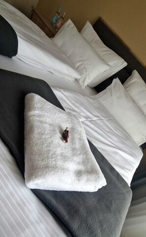 A neatly made bed with white linens, a gray blanket, and a decorative item on the pillow.