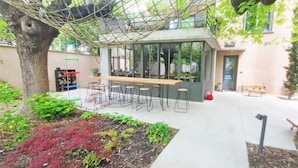 A modern outdoor seating area with a wooden table and chairs, surrounded by greenery and a rope swing. - Villa Piscine, Jardin Arboré, Proche Centre Ville (Montélimar)