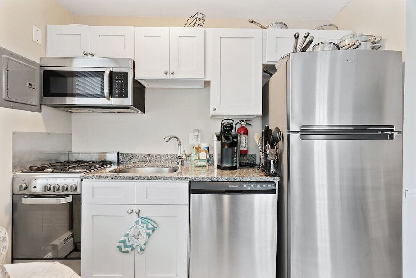 A modern kitchen with stainless steel appliances, white cabinets, and a granite countertop.