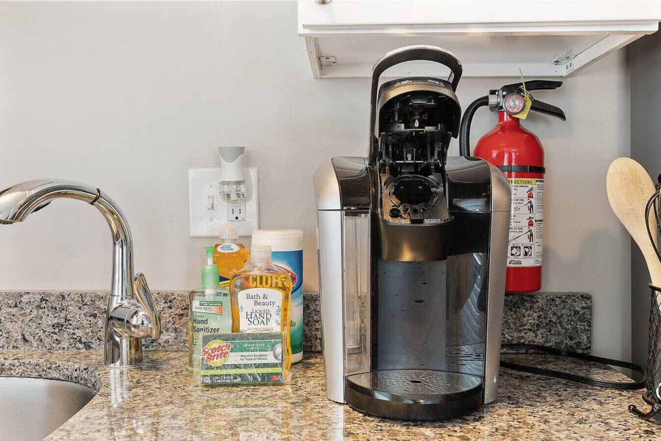 A kitchen with a coffee maker, hand sanitizer, and a fire extinguisher.