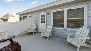 Un edificio con un patio techado, que incluye sillas Adirondack blancas y un banco de madera.