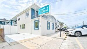 Un edificio de dos pisos con un letrero que dice 'SALTY SHORE', un camino de entrada con portón y un SUV blanco estacionado.