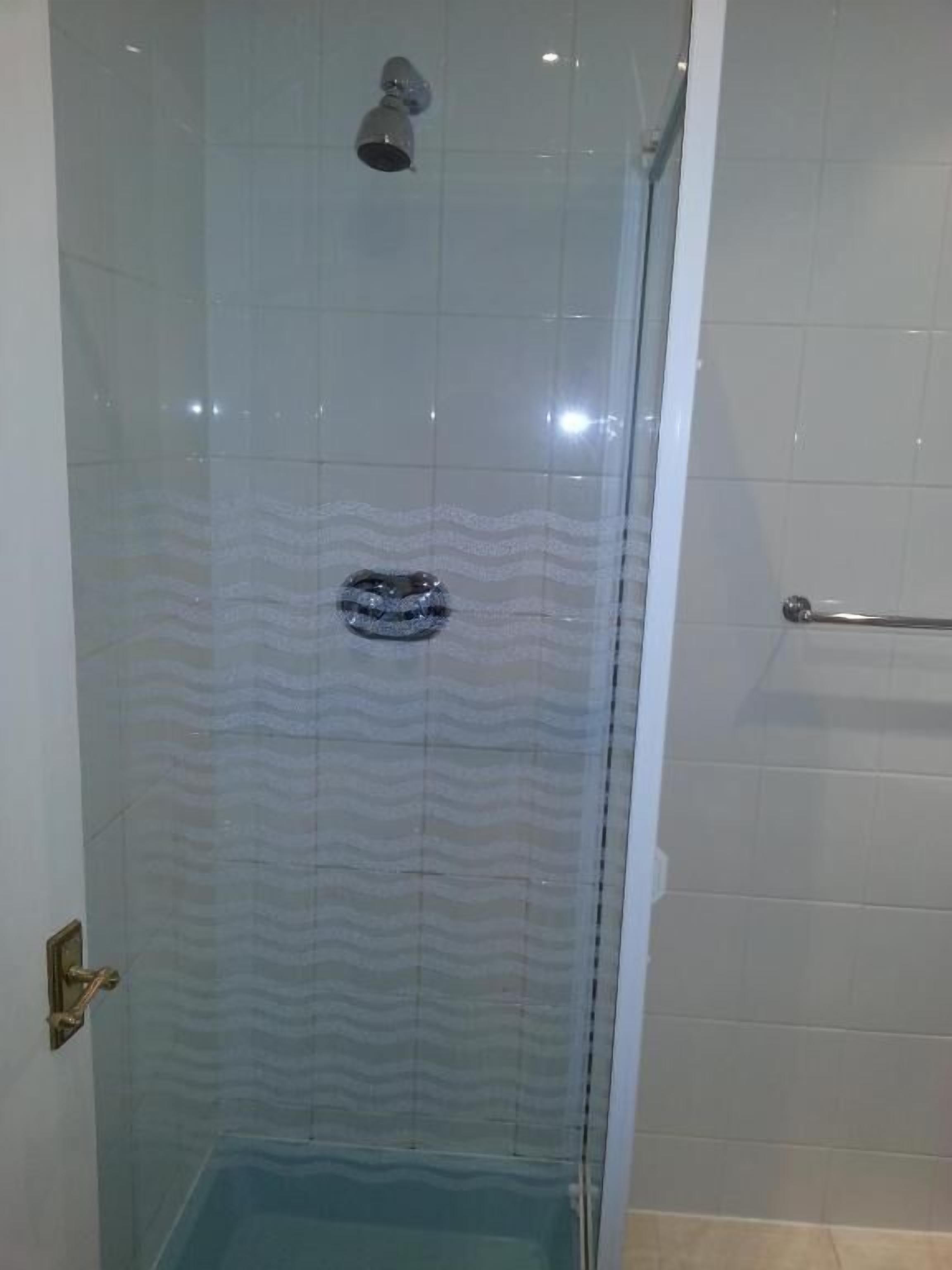 Une douche fermée par des parois en verre, dotée d’une poignée en métal et d’un drain visible.