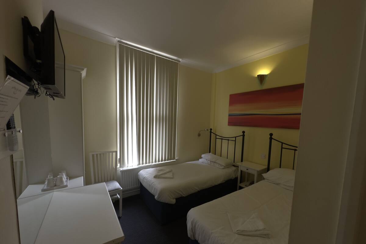 A hotel room with two beds, a desk, a chair, a TV, and a window with blinds.