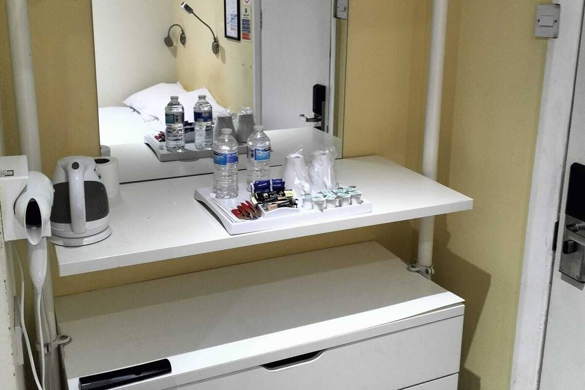 A hotel room with a white desk, a mirror, a kettle, and a minibar.