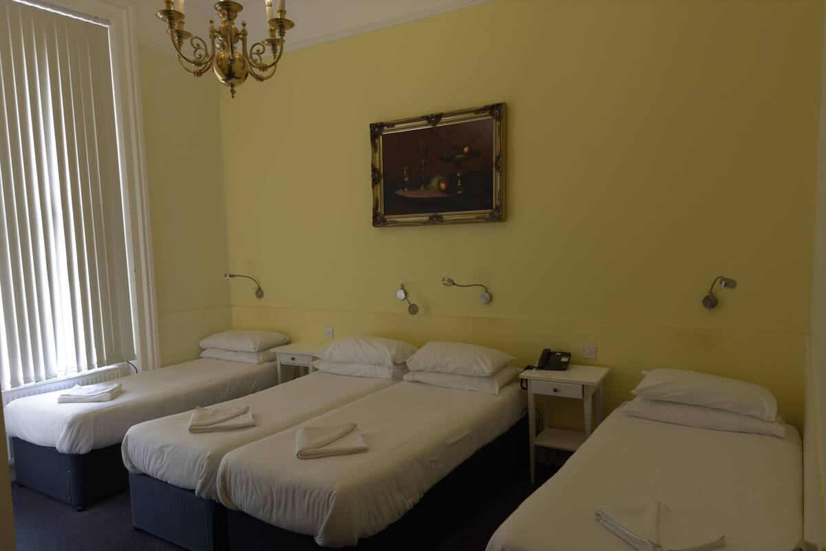 A hotel room with three single beds, a chandelier, a painting on the wall, and bedside lamps.