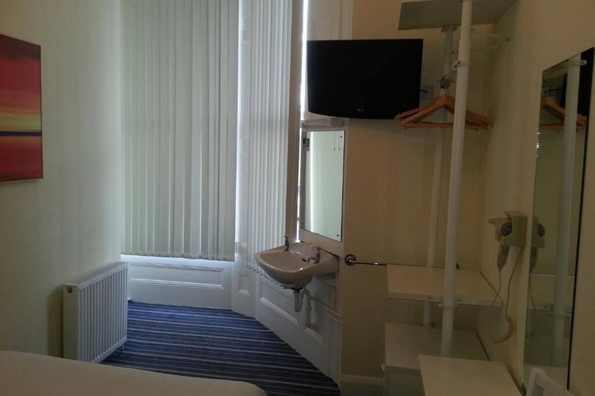 A hotel room with a large bed, a flat-screen TV mounted on the wall, a sink, and a mirror.