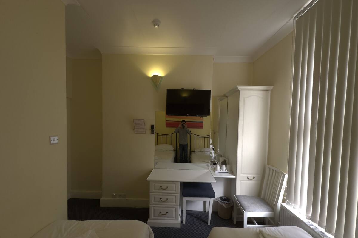 A hotel room with two beds, a desk, a chair, a TV, and a window with blinds.