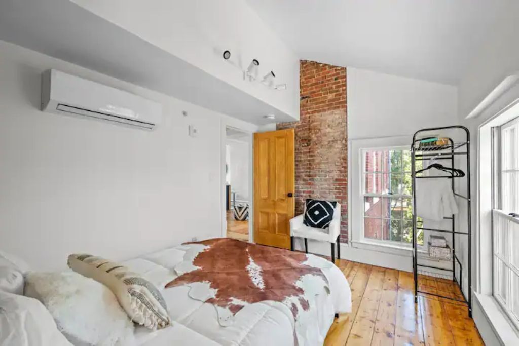 A bedroom with a bed, a brick wall, a window, and a metal rack.