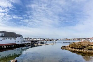 A waterfront building with a dock extending into calm water, surrounded by a small rocky outcrop and a clear sky. - 3BR Harborside Home • Gloucester+Rockport • Ocean View (Gloucester)