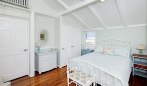 Un dormitorio con cama blanca, mesita de noche, cómoda y ventana con vistas.