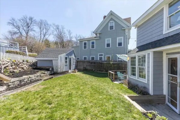 A residential property with a well-maintained lawn, a stone retaining wall, and a wooden deck. - 3BR Harborside Home • Gloucester+Rockport • Ocean View (Gloucester)