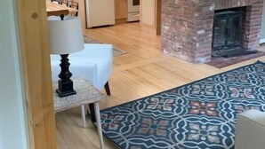 A modern kitchen with wooden cabinets, a brick fireplace, and a dining area with a table and chairs. - Four Winds Cottage (Southwest Harbor)