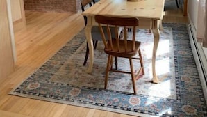 A dining area with a wooden table and chairs, a rug, a brick wall, and a hanging light fixture. - Four Winds Cottage (Southwest Harbor)