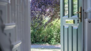 Eine geöffnete Tür, die zu einem Garten mit dichtem Grün und einem Metallgitter führt.