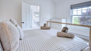 Ein Schlafzimmer mit karierter Bettdecke, einem Holz-Kopfteil und Blick auf einen Garten durch ein Fenster.