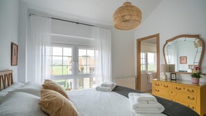 A bedroom with a large bed, a dresser, a mirror, and a window with curtains. - Montealmar Galizano Somo (ribamontan al mar)