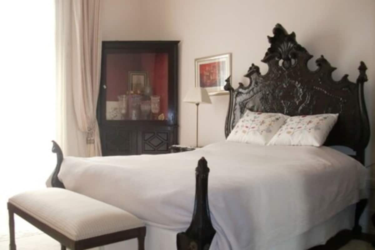 A bedroom with a large bed, a nightstand, a dresser, and a window with curtains.