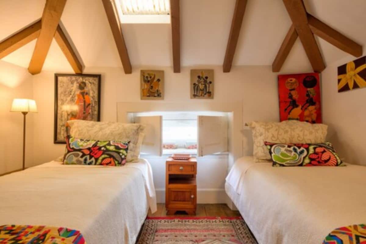 A bedroom with two beds, a wooden nightstand, and a window with a view.