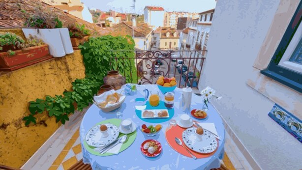 Una mesa redonda con mantel de encaje, rodeada de platos de comida, tazas y un florero con flores.