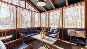 A cozy room with a wooden ceiling, large windows, a sofa, chairs, a table, and a relaxation station. - Private Wooded Escape + Hot Tub + Fire Pit and Screen Porch (East Stroudsburg)