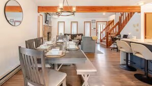 A spacious dining area with a long table set for a meal, a cozy seating area with a sofa, and a staircase leading to an upper level. - Private Wooded Escape + Hot Tub + Fire Pit and Screen Porch (East Stroudsburg)
