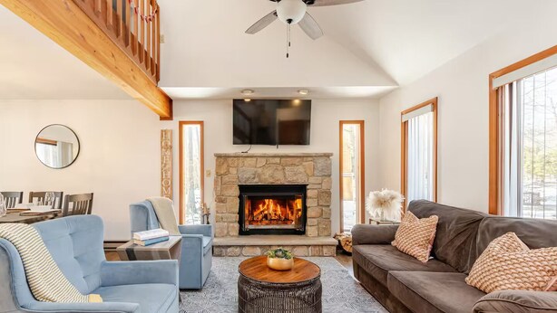 A modern living room with a stone fireplace, a ceiling fan, and large windows. - Private Wooded Escape + Hot Tub + Fire Pit and Screen Porch (East Stroudsburg)