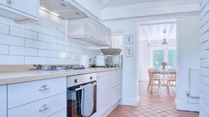 Una cocina moderna con armarios blancos, horno empotrado y comedor con mesa y sillas.