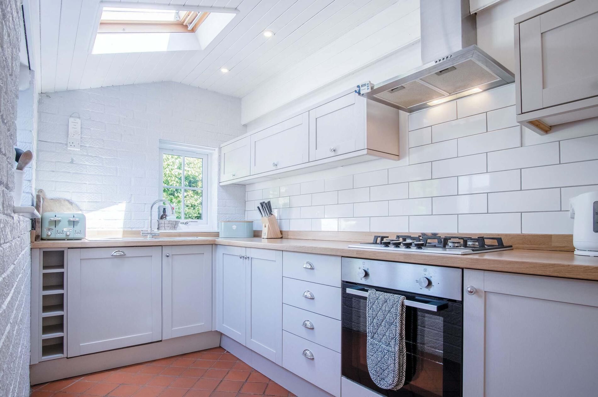 Een moderne keuken met witte kasten, een gasfornuis en een raam dat natuurlijk licht binnenlaat.