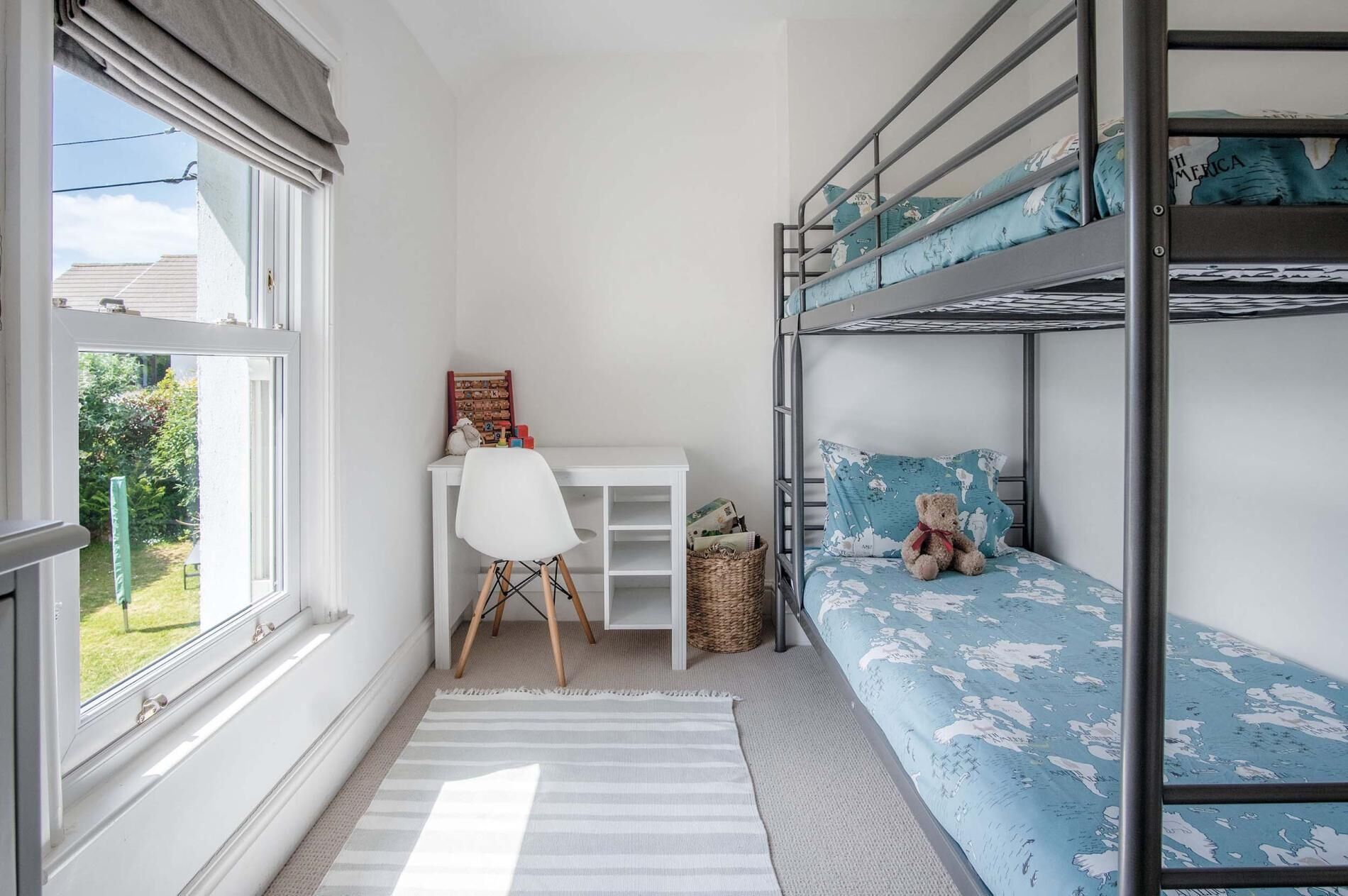 Camera da letto per bambini con letti a castello, una scrivania e una finestra che si affaccia sul verde.