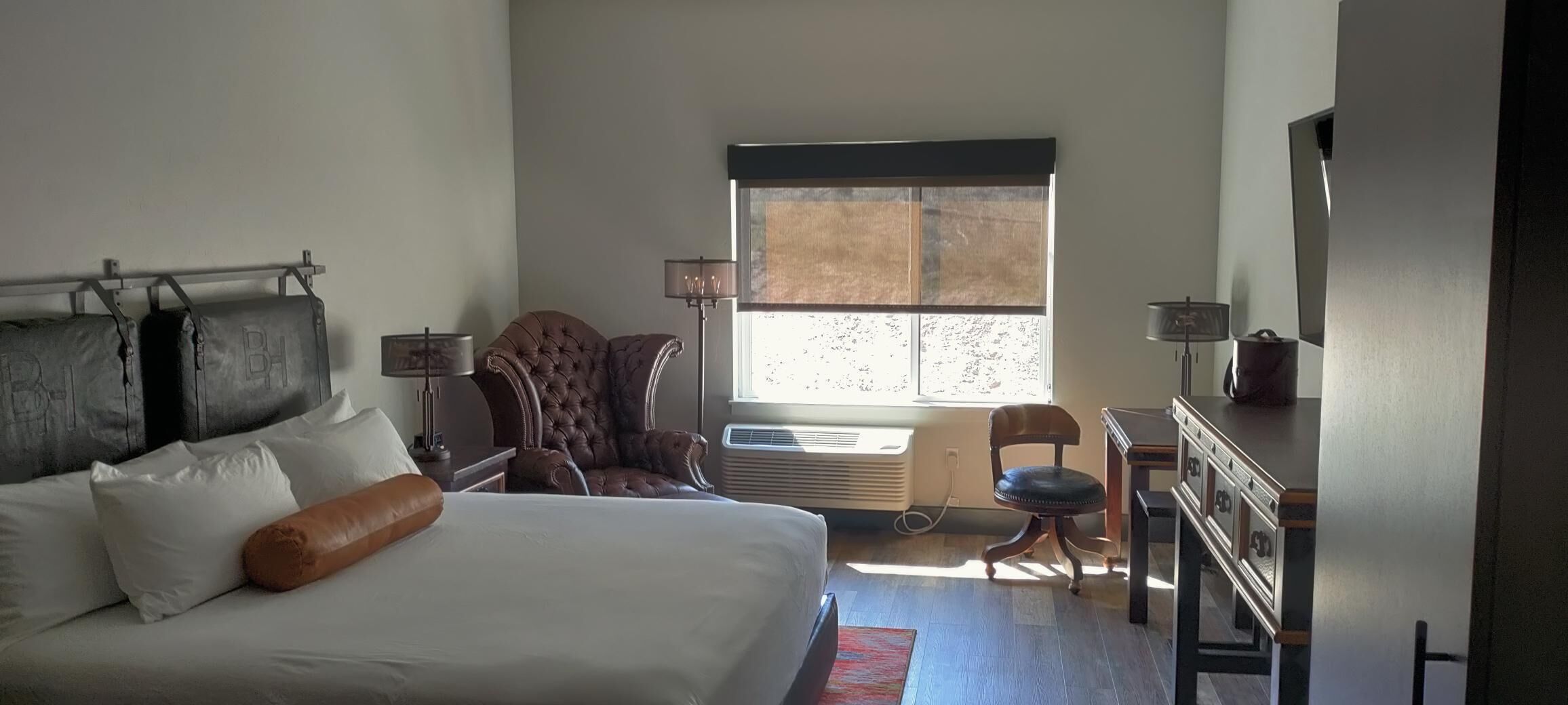Ett hotellrum med en stor säng, en stol, ett skrivbord och ett fönster.
