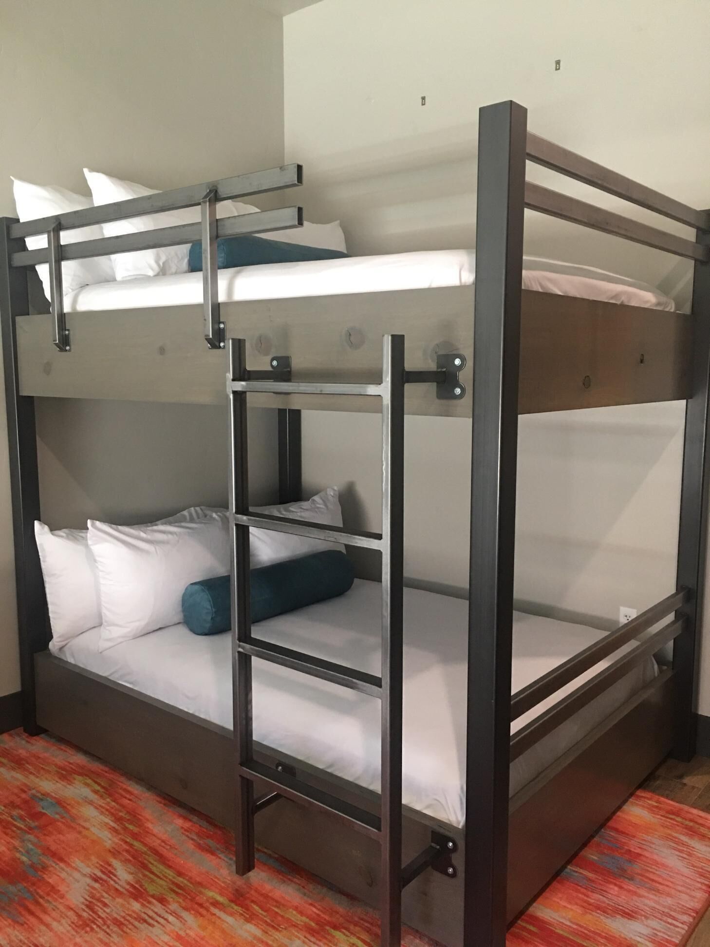 A bunk bed with a ladder, white bedding, and a colorful rug.