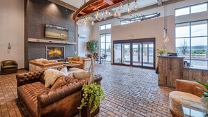 A spacious lobby with a brick floor, leather sofas, a fireplace, and large windows offering a view. - The Bunk House at Cross Keys (Madras)
