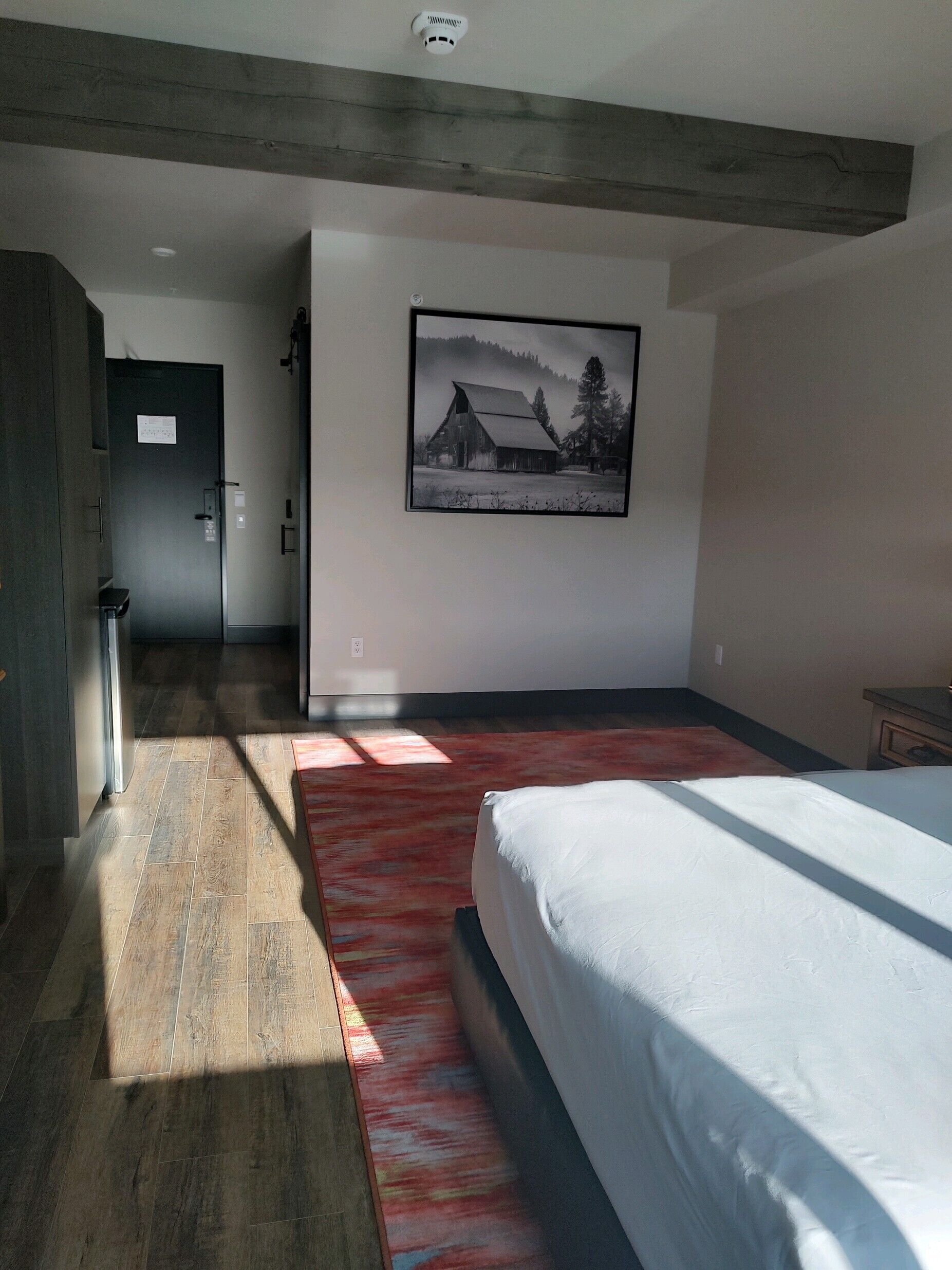 Un dormitorio con una cama grande, piso de madera, un tapete rojo y un cuadro de una casa en la pared.