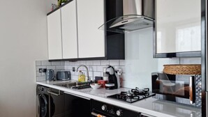 Une cuisine moderne avec des meubles blancs, un lave-vaisselle, une cuisinière à gaz et une machine à café.
